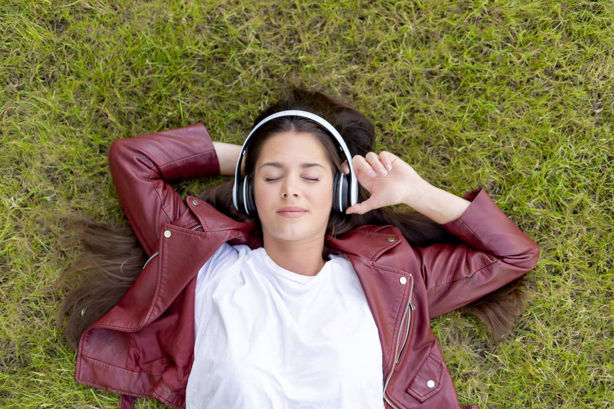 Woman lying on grass listening with headphones — brainwave audio