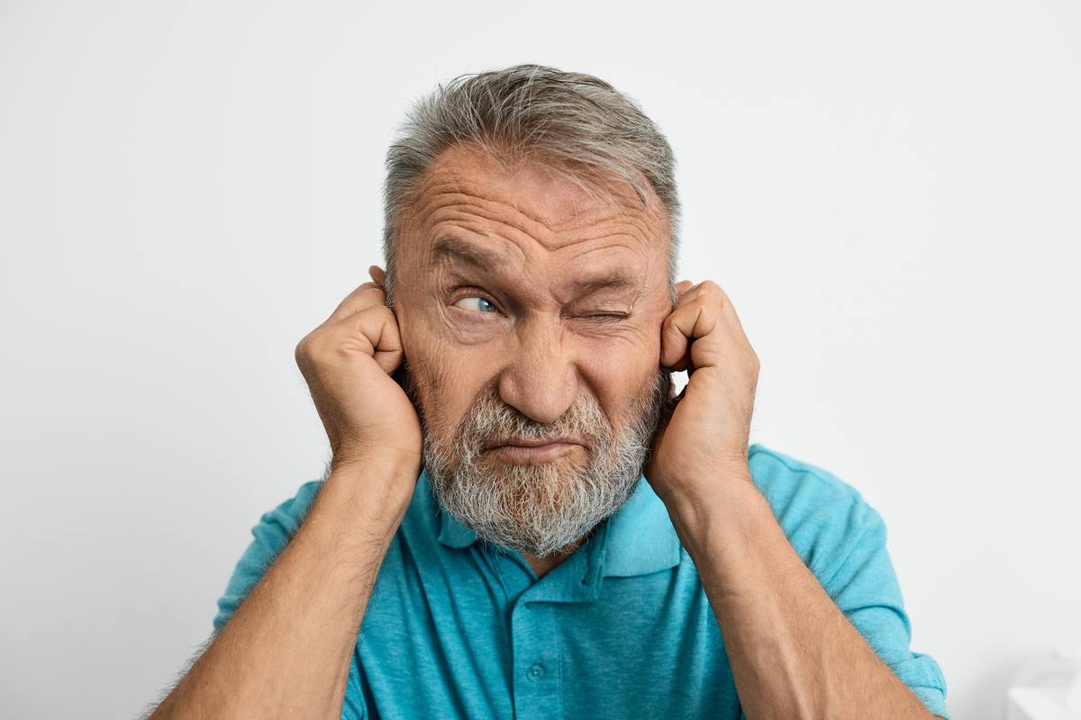Senior man covering ears from tinnitus ringing